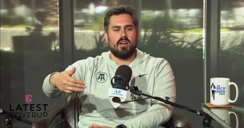 A bearded man sits in front of a microphone, discussing topics related to Big Cat’s Family.