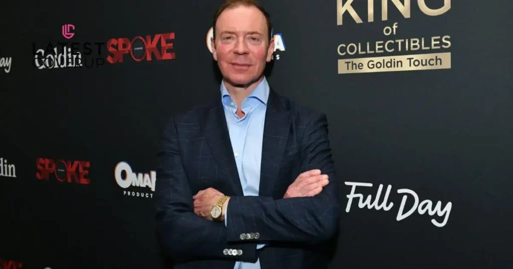 A man in a suit and tie stands on a red carpet, symbolizing success and elegance, reflecting Ken Goldin's net worth.