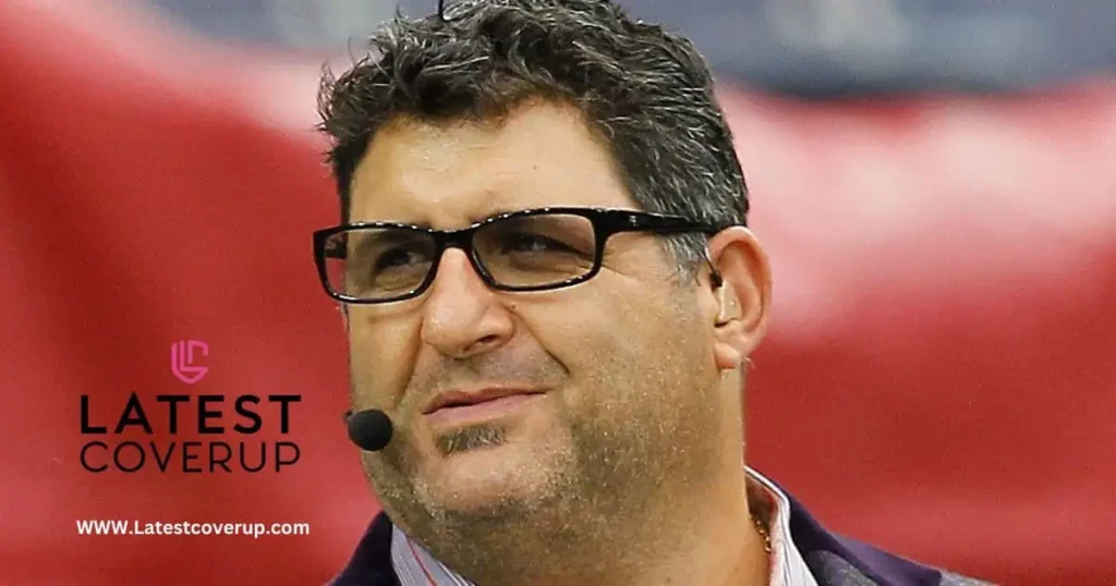 A man in glasses and a tie speaks into a microphone, discussing topics related to Tony Siragusa's net worth.