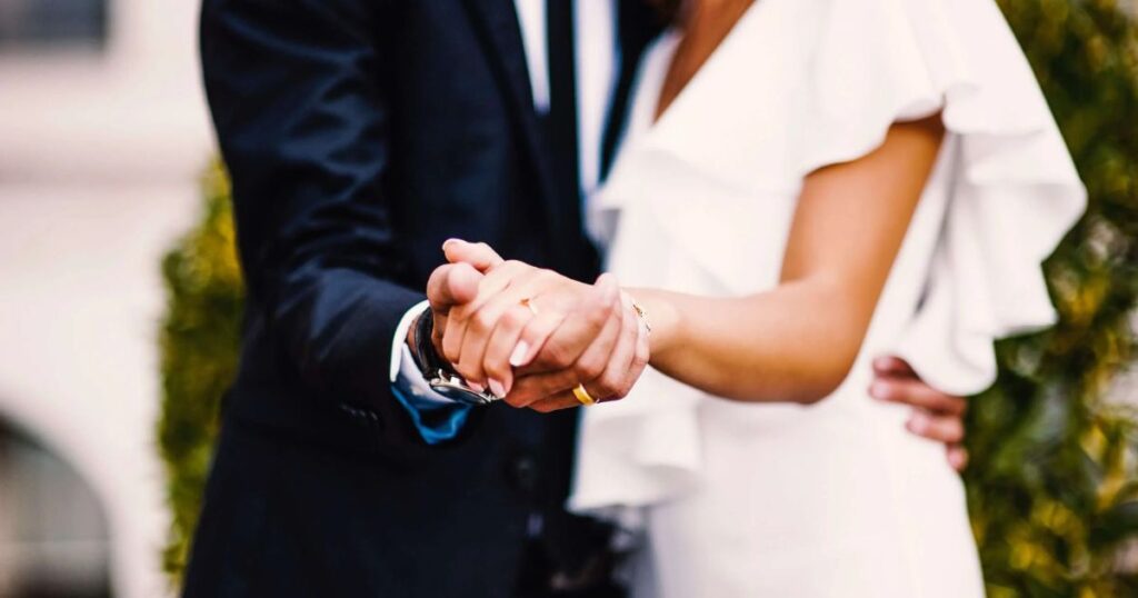 A man and woman holding hands in front of a building, symbolizing Tony Hinchcliffe's relationship and connection.