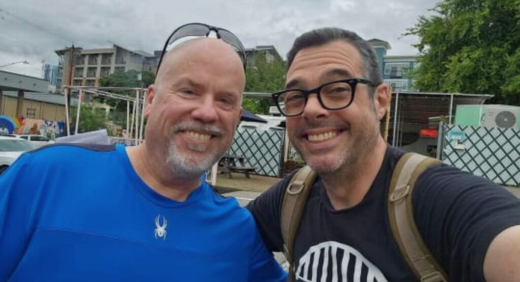 Two men smile for the camera in front of a building, showcasing their camaraderie and discussing Aaron Franklin Rise and carear.