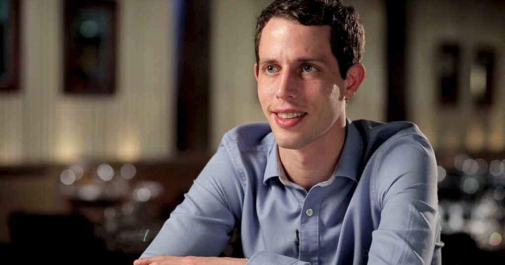  A man in a blue shirt, identified as Tony Hinchcliffes, is seated at a table, engaged in conversation.