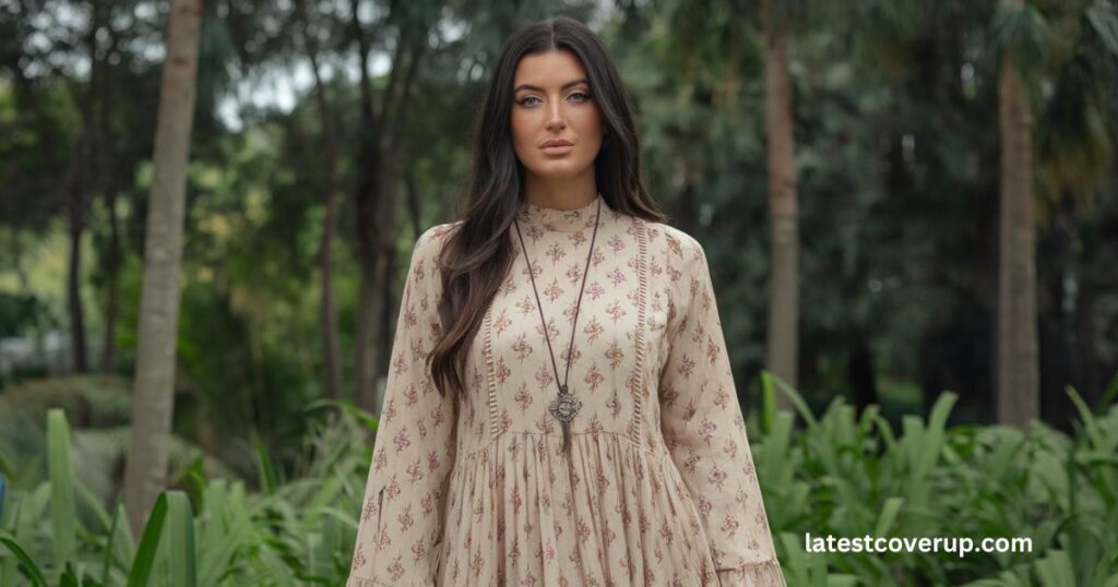 A woman in a beige dress stands gracefully in a field, embodying the essence of nature and beauty, who is Jyleen's wife.